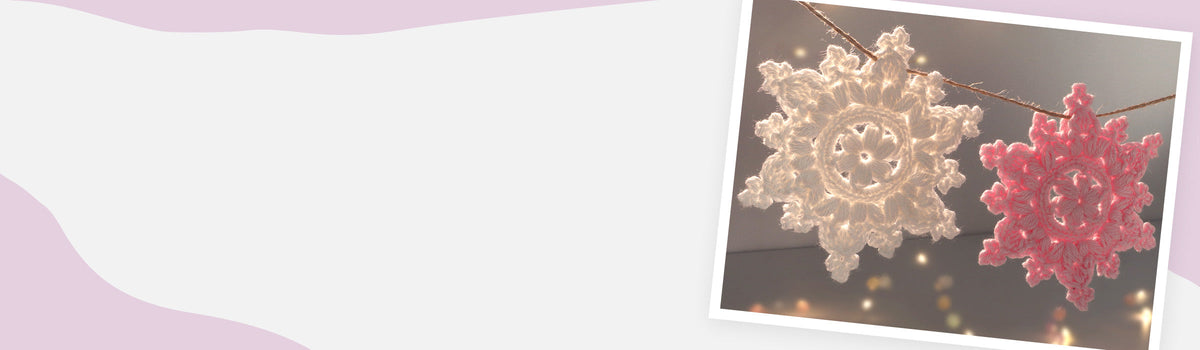 Zwei gehäkelte Schneeflocken (weiß und rosa) hängen an einer Schnur – Banner für Schneeflocken häkeln - Häkelanleitungen