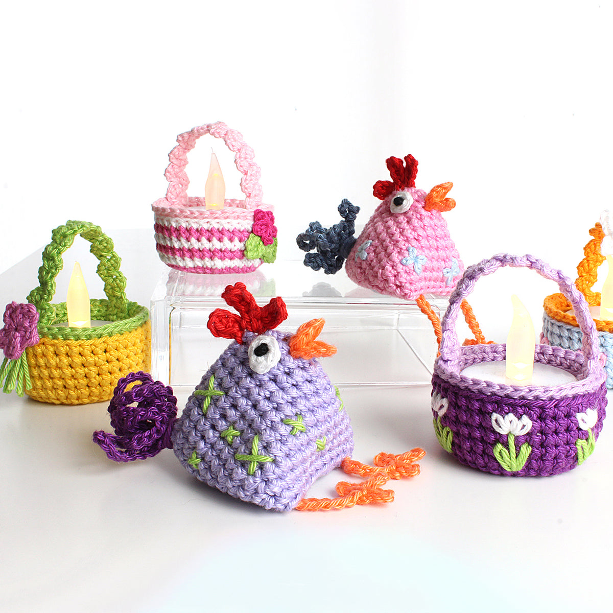 Bunte gehäkelte Hühner und kleine bestickte Körbchen mit Henkeln und leuchtenden LED-Teelichtern als Osterdeko.