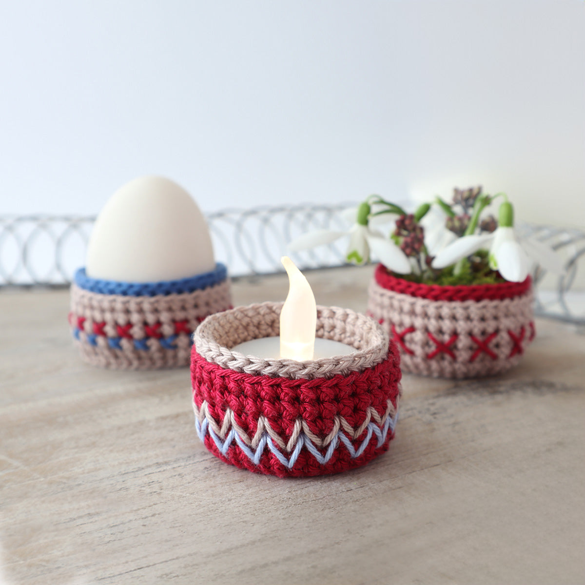 Gehäkelte kleine Körbchen in Rot und Blau, eines mit LED-Teelicht und eines als Eierbecher mit weißem Ei.