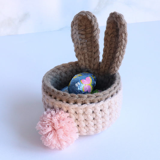 Gehäkelter Hasenkorb in Rosa und Braun mit langen Ohren, rosa Verzierung und buntem Osterei.