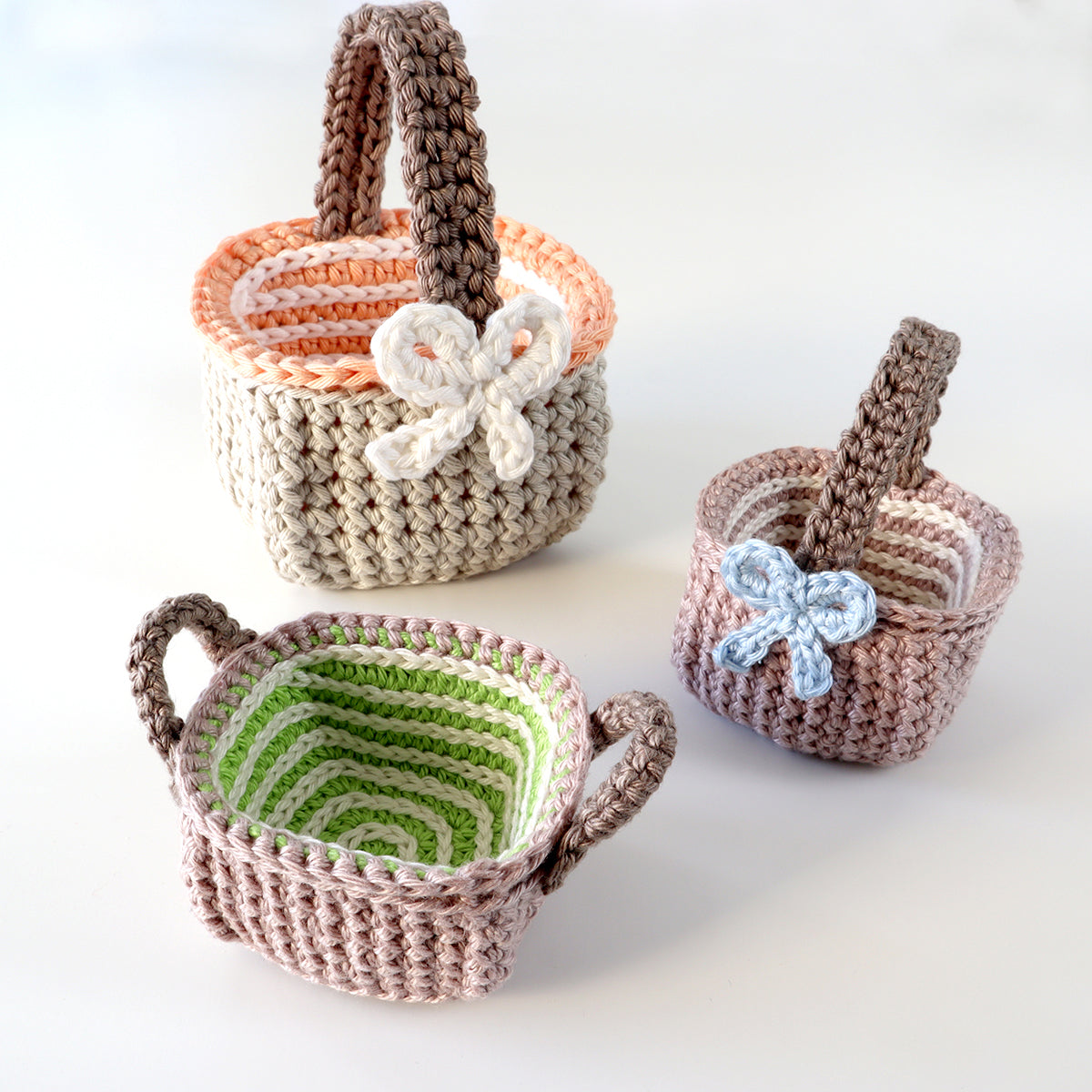 Drei gehäkelte Körbchen „Spirelli“ in Natur-, Orange-, Mint- und Grüntönen mit Henkeln und dekorativem Spiralboden