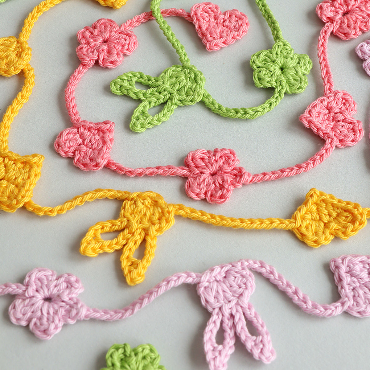 Gehäkelte Ostergirlanden in Gelb, Rosa und Grün mit Hasen-, Herz- und Blümchenmotiven auf hellem Untergrund.