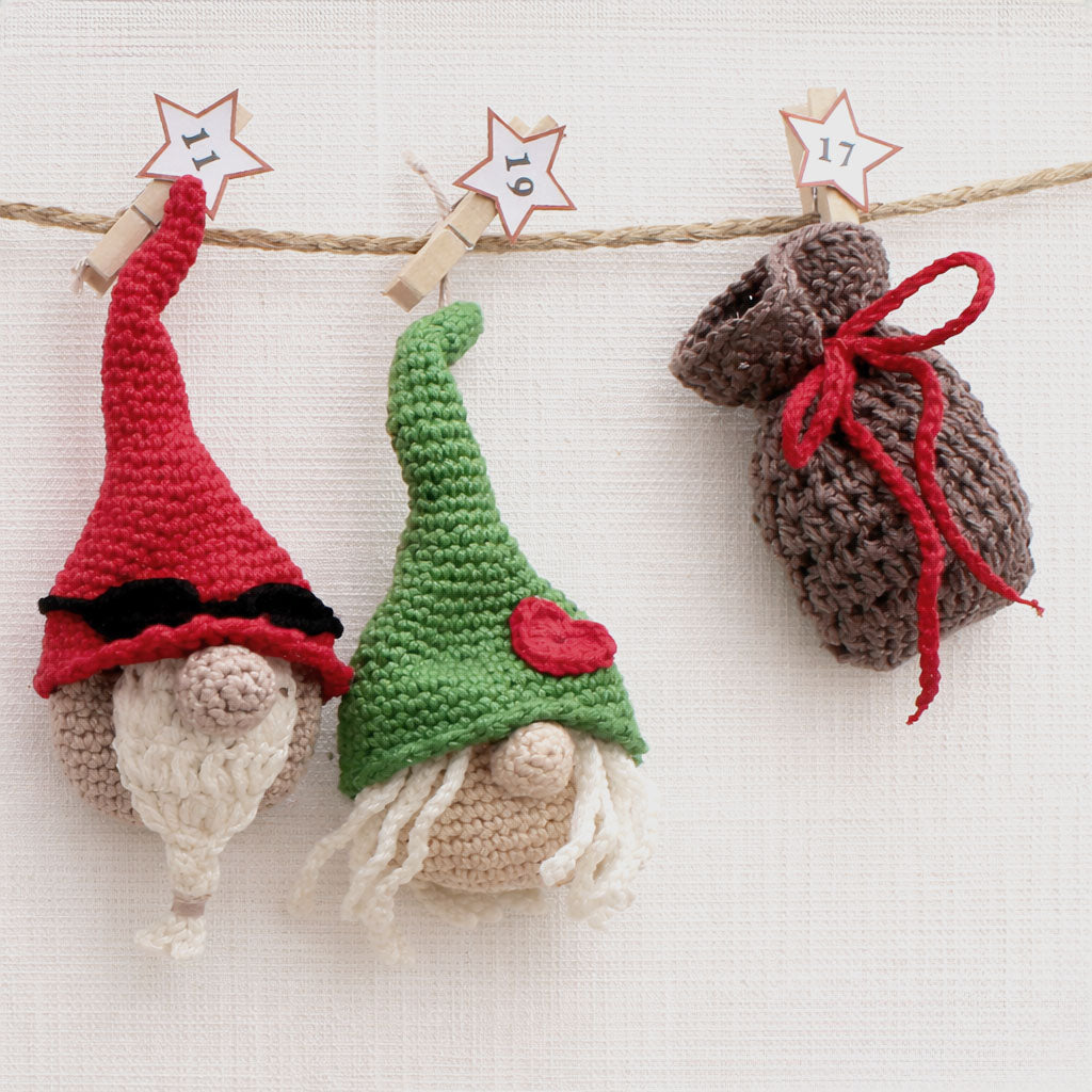 Zwei gehäkelte Weihnachtswichtel in Rot und Grün mit einem befüllbaren Säckchen als Weihnachtsdeko.