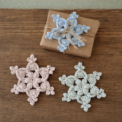 Gehäkelte Schneeflocken „Lucy“ in Hellblau, Rosa und Mint auf einem Holzuntergrund